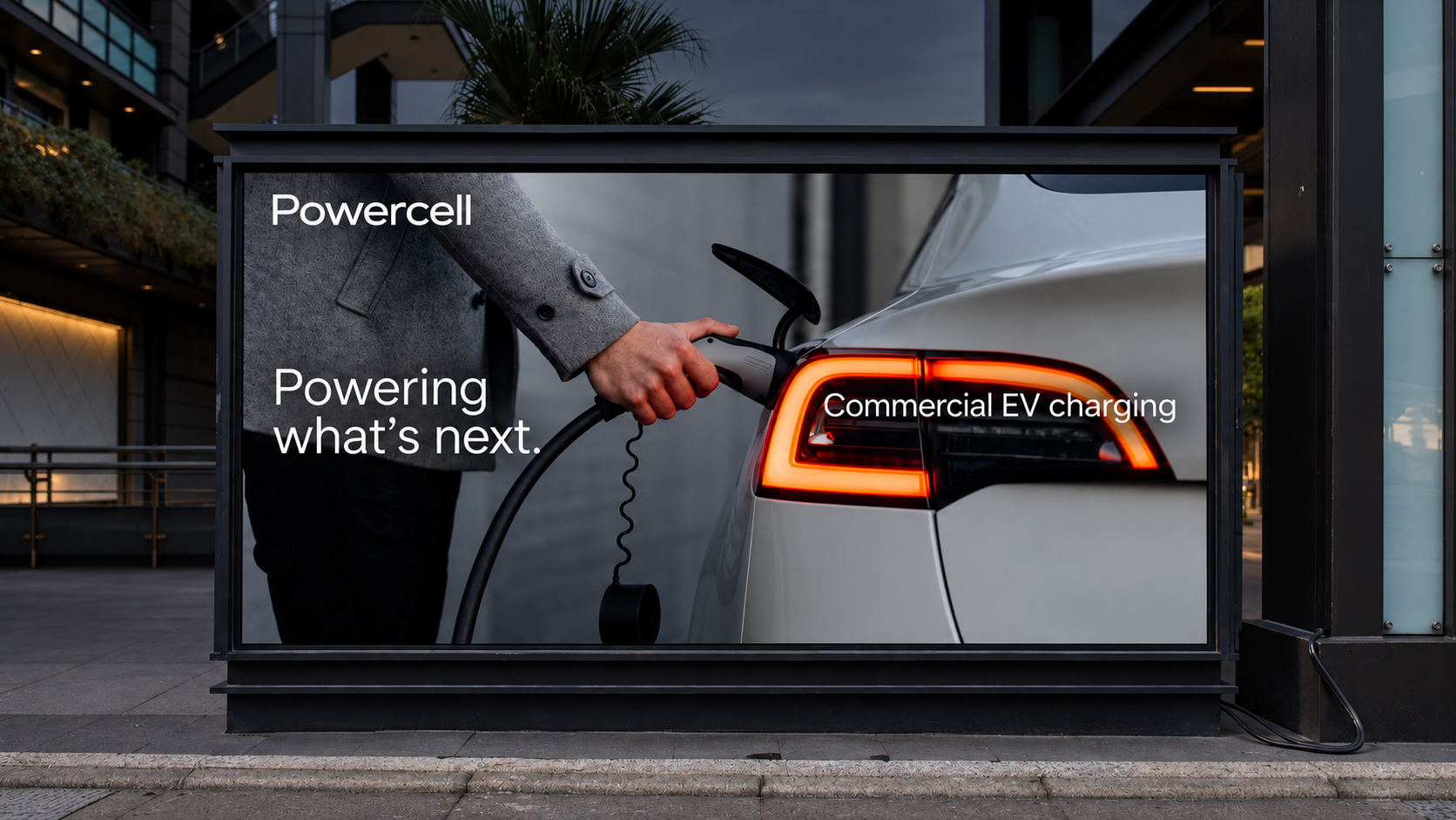 Powercell billboard showing a driver plugging in a silver electric car, with the message Powering what’s next. Commercial EV charging.